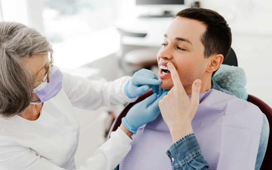 Dentist examining a patient’s mouth while the patient points to a painful tooth during a dental checkup.