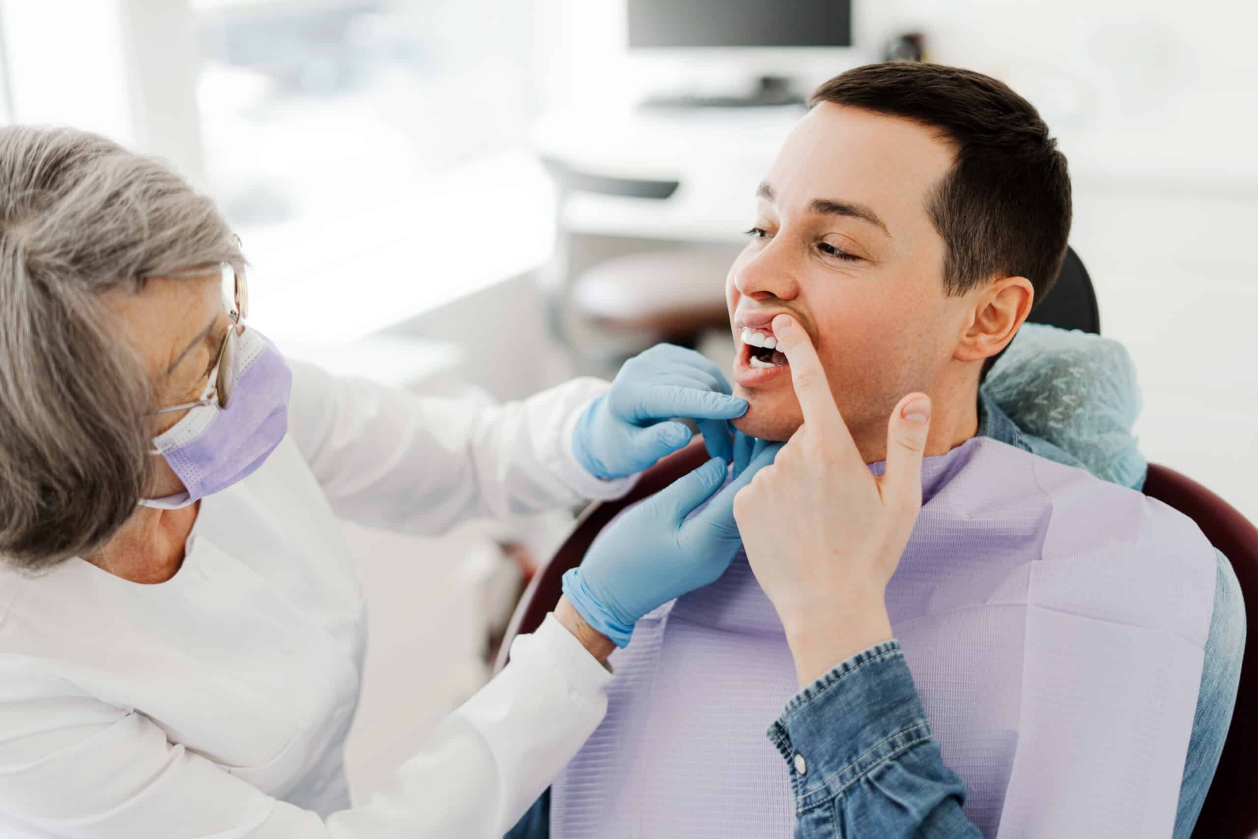 Dentist examining a patient’s mouth while the patient points to a painful tooth during a dental checkup.