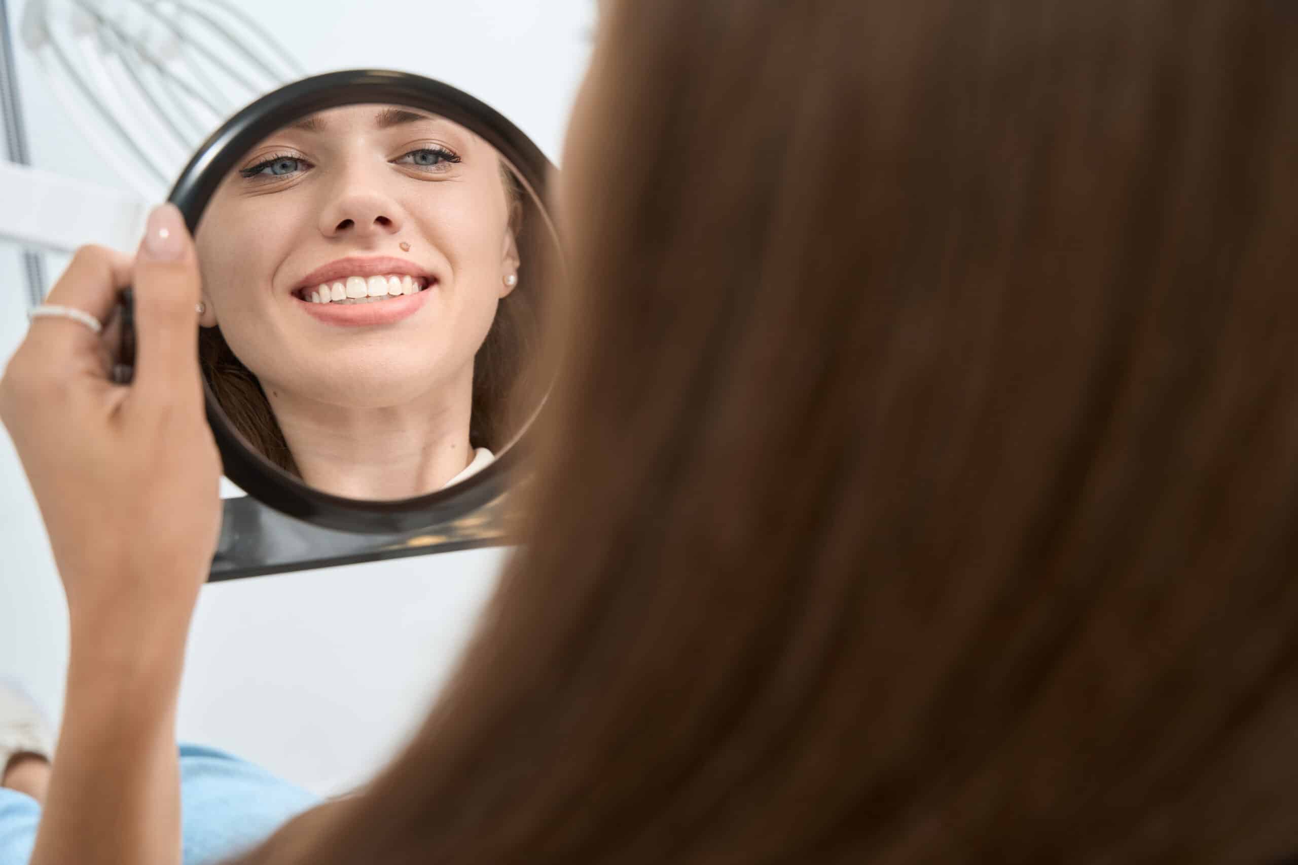 Patient smiling while looking at her teeth in a mirror after cosmetic dental treatment.