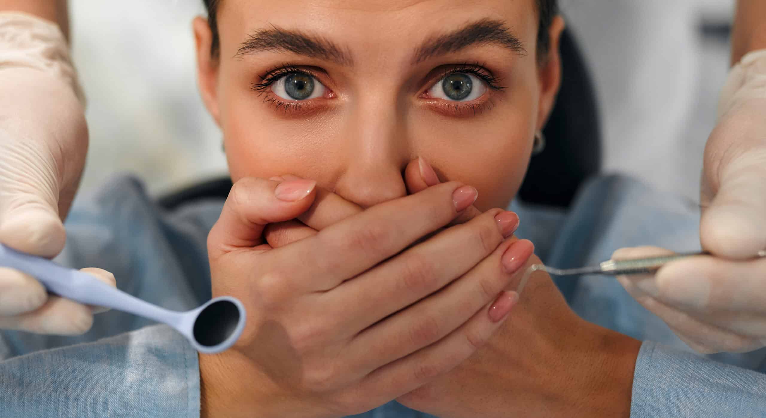 Anxious patient covering her mouth while a dentist holds dental instruments during an appointment, illustrating fear of dental treatment.