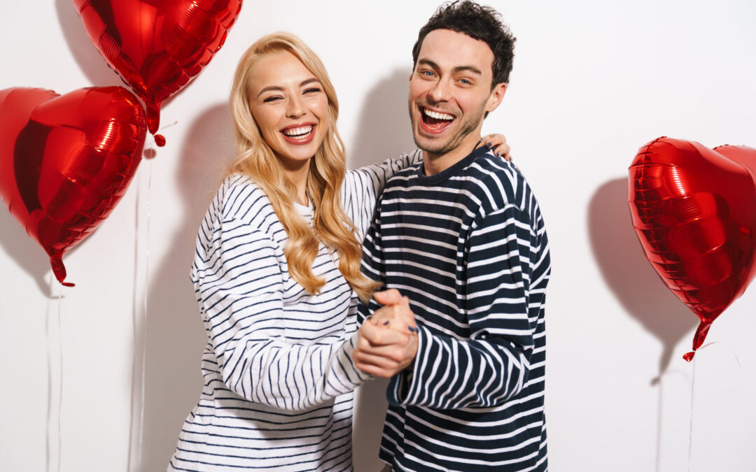 Smiling couple celebrating Valentine’s Day with bright, healthy smiles and red heart balloons in the background
