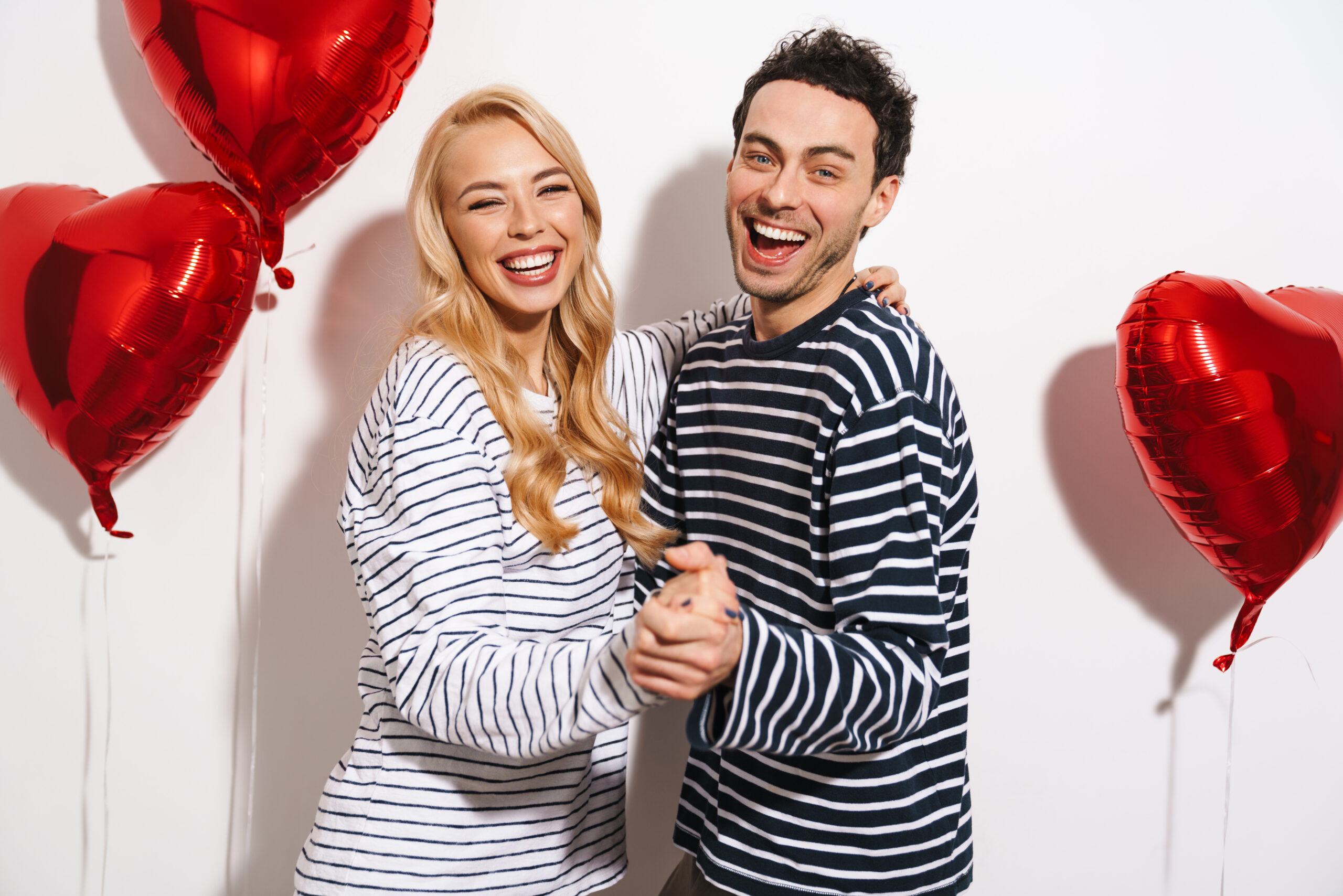 Smiling couple celebrating Valentine’s Day with bright, healthy smiles and red heart balloons in the background