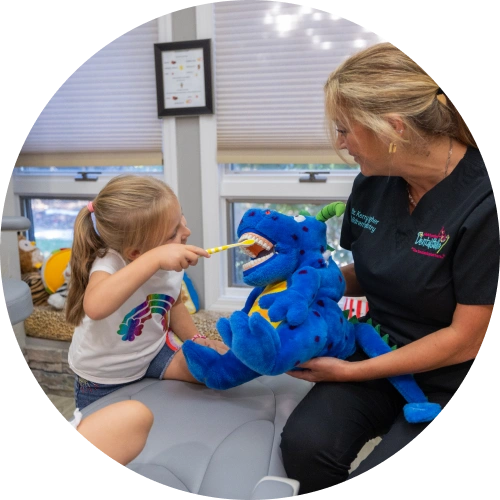 Young child brushing teeth of blue puppet with dentist in dental office setting.