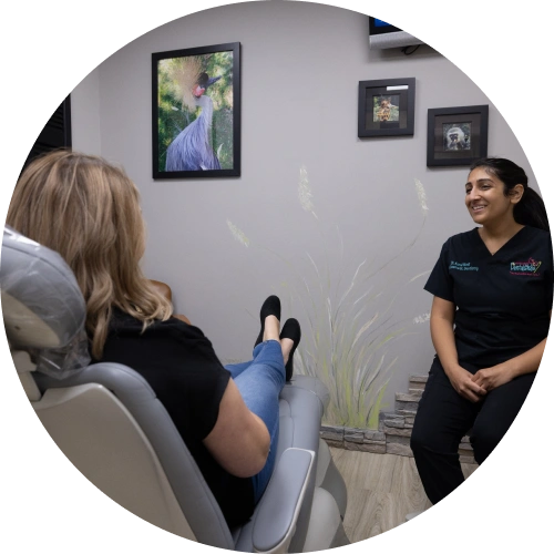 Dental professional in black scrubs consults with patient in modern dental office treatment room.