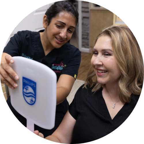 Two women smiling while holding a Philips dental device in a clinical setting.