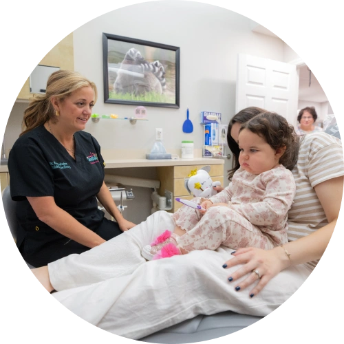 Pediatric dentist examining young child patient in dental office treatment room.