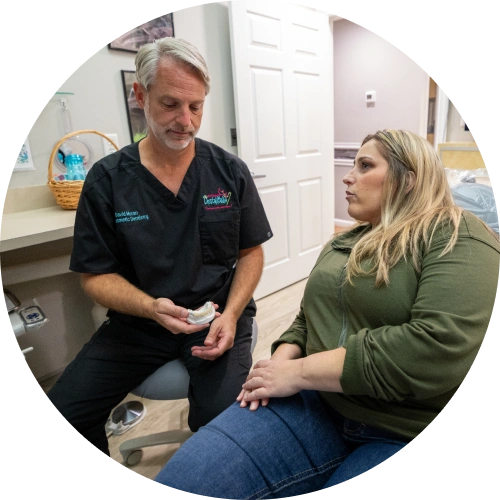 Dentist in black scrubs consulting with female patient in dental office examination room.