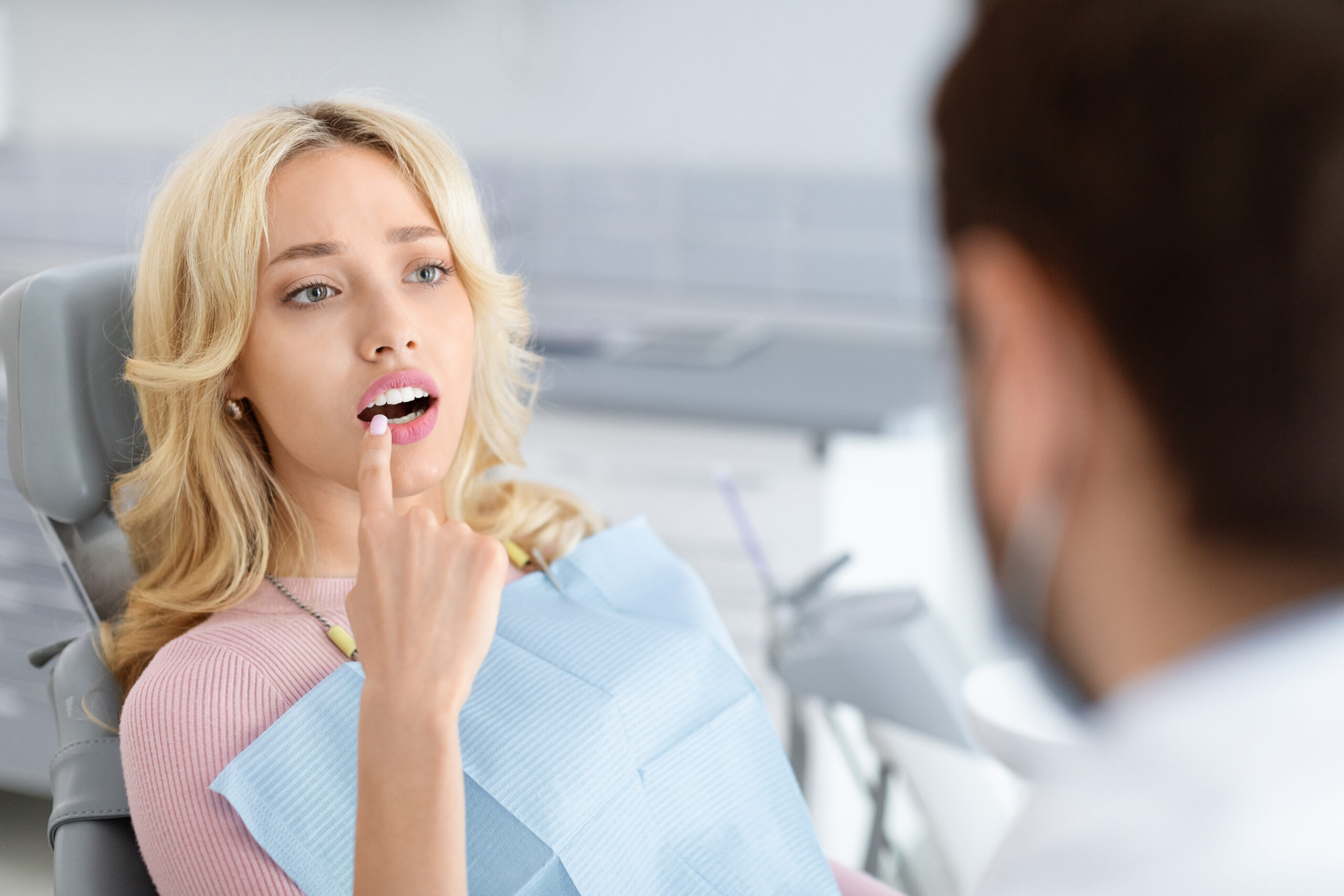 Woman pointing to slightly misaligned tooth during dental consultation, discussing cosmetic smile correction options