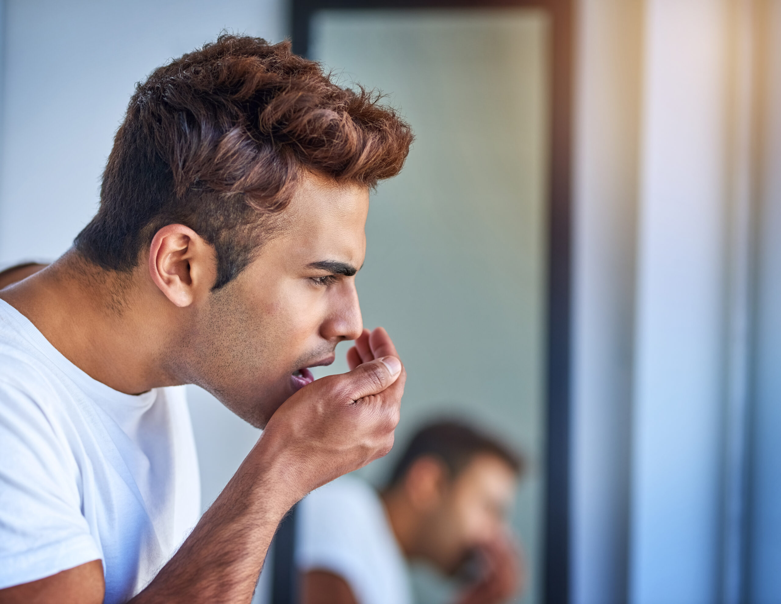 Man checking his breath in the mirror, concerned about bad breath and oral hygiene