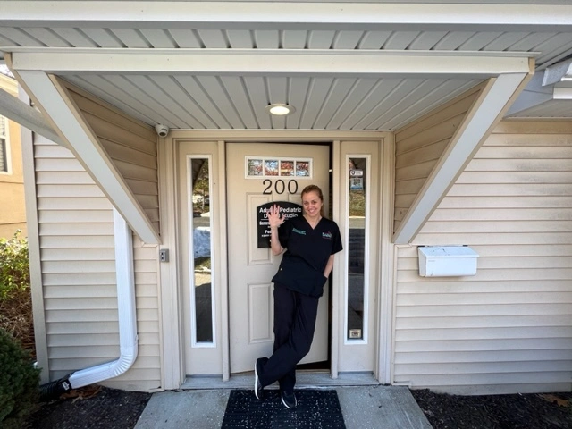 Friendly dental team member waving at the entrance of Adult & Pediatric Dental Studio in Manalapan, NJ