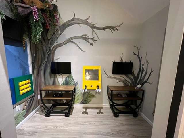 Child friendly waiting room at Adult & Pediatric Dental Studio featuring a nature-themed mural with a tree, kids' activity stations, and TVs