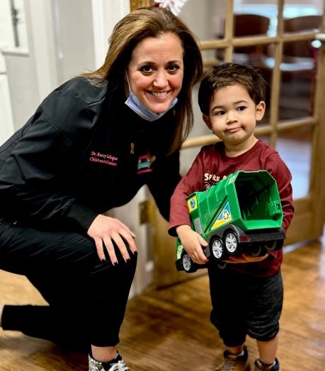Pediatric dentist smiling next to a young child holding a toy truck