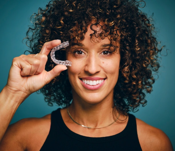 Smiling adult woman holding a clear plastic orthodontic aligner