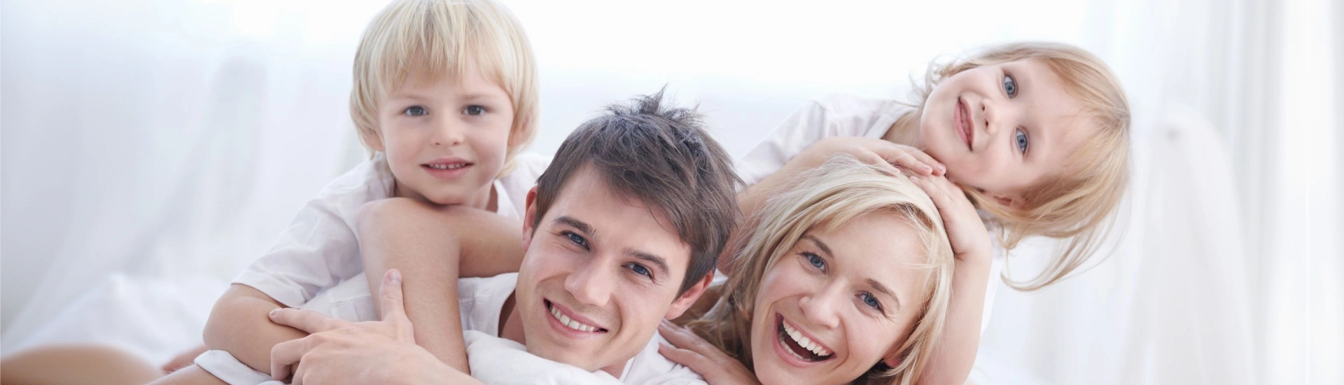 A cheerful mother, father, and their two young kids piling on top of each other and laughing