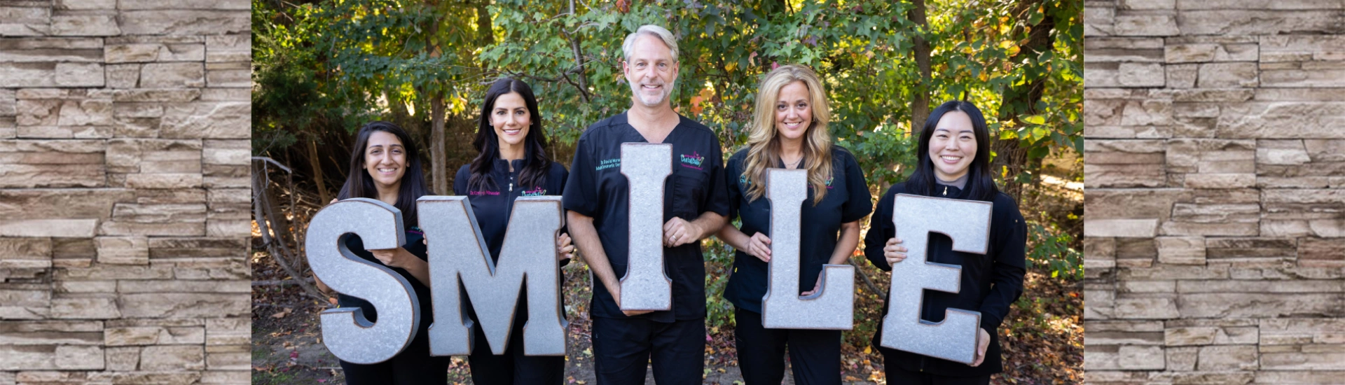 Five dental staff members standing outdoors holding large letters that spell "SMILE"