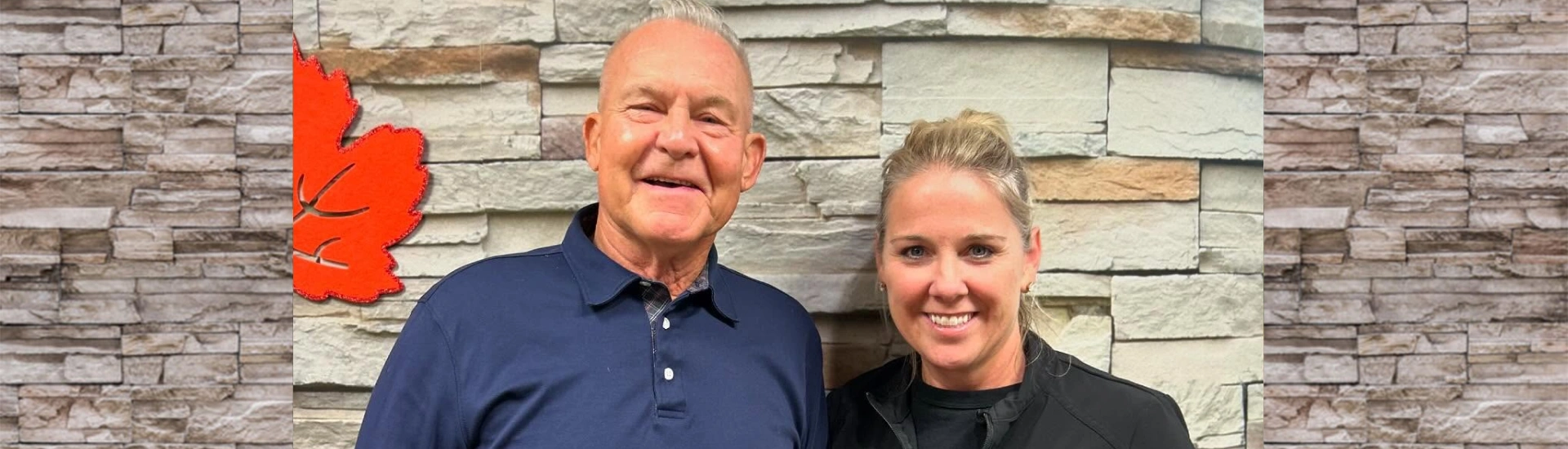 A smiling mature man and a woman posing closely together in front of a stone wall background