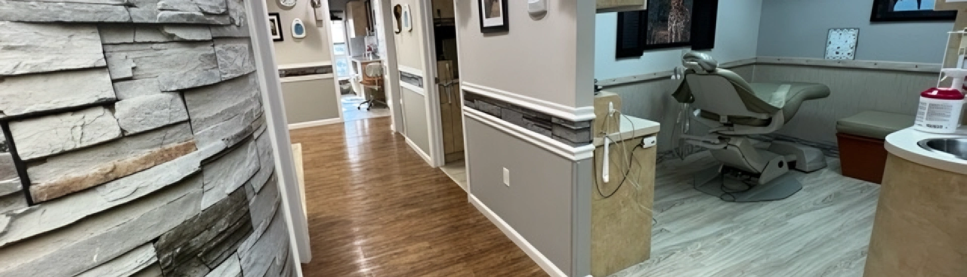 An interior view showing a dental office hallway with wood flooring leading into a clean clinical treatment room