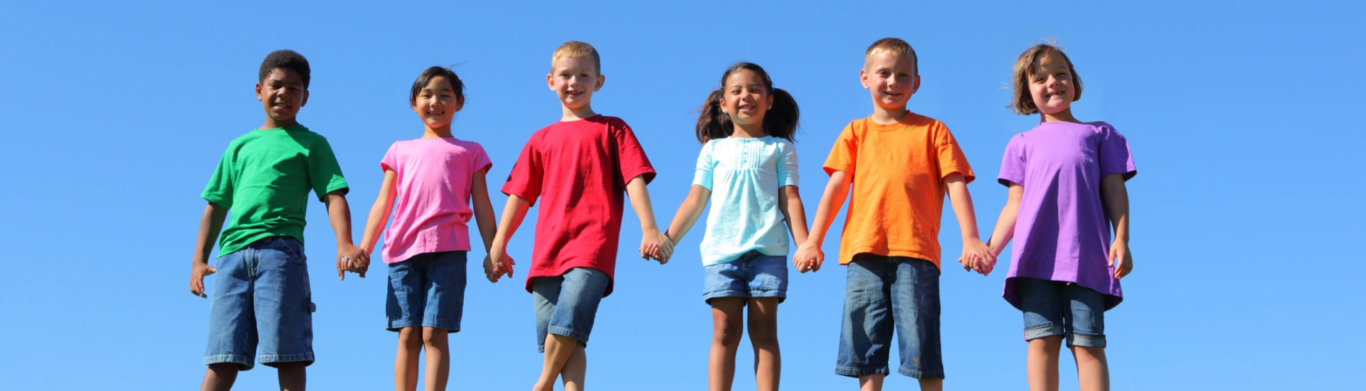 Six happy young children wearing brightly colored t-shirts standing together outside