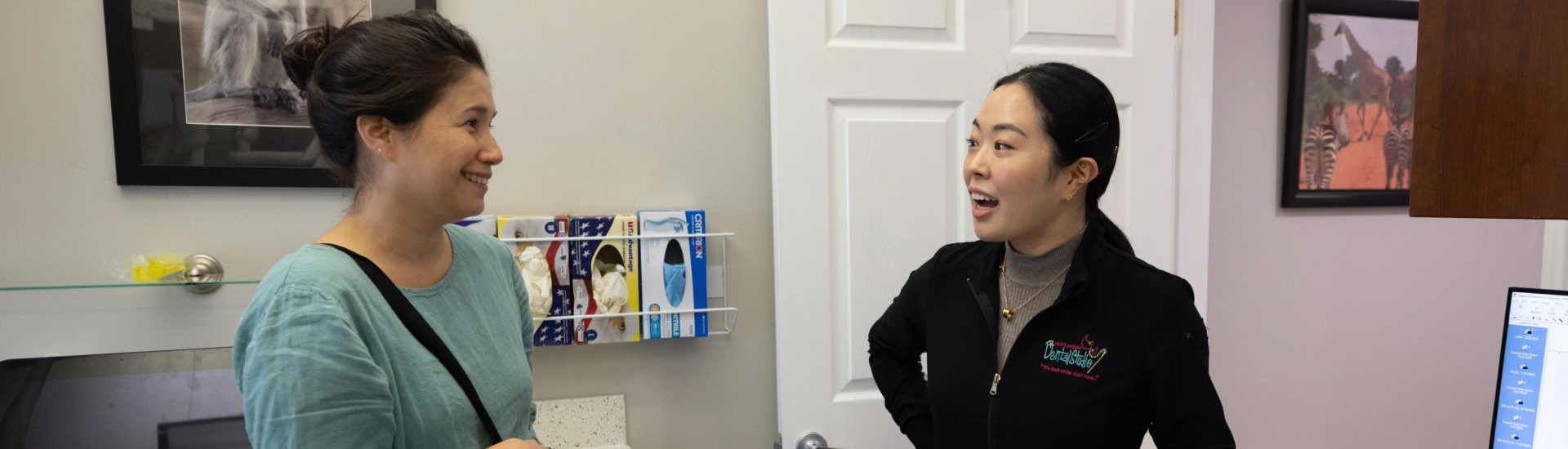 A dental staff member speaking with a smiling patient inside an office