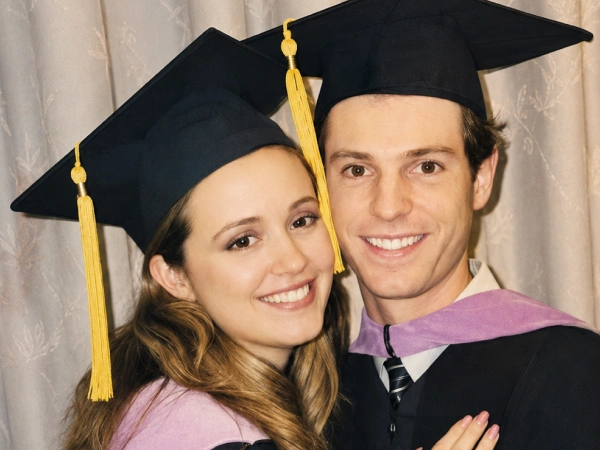 Graduates in caps and gowns smiling for a portrait.
